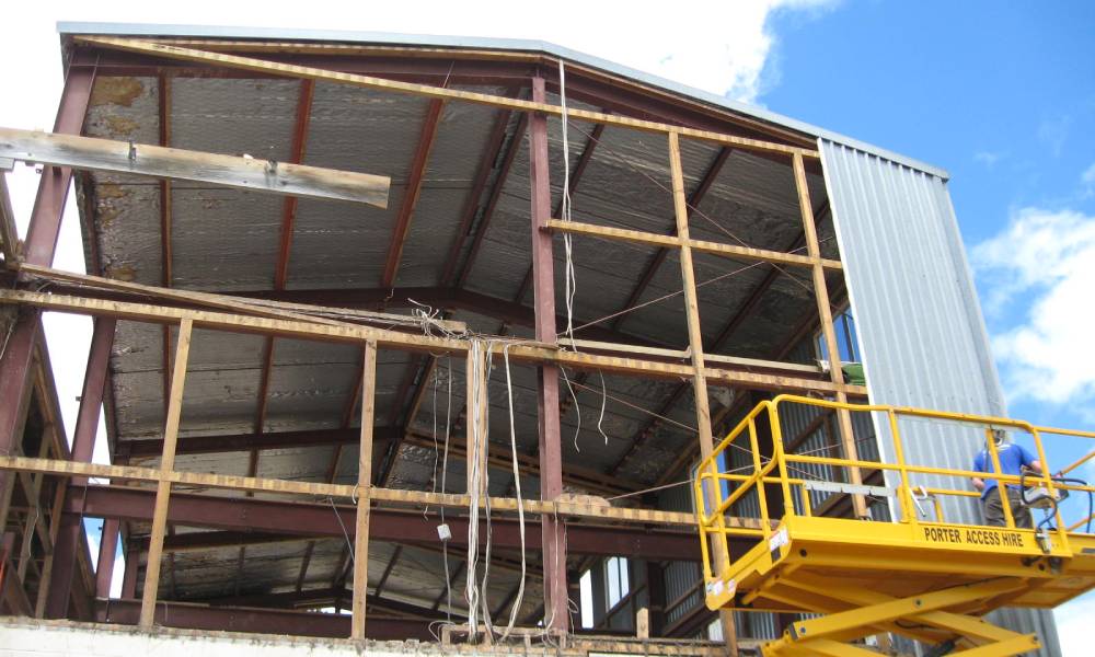 A worker on a scissor lift removing corrugated iron off the side of a commercial building