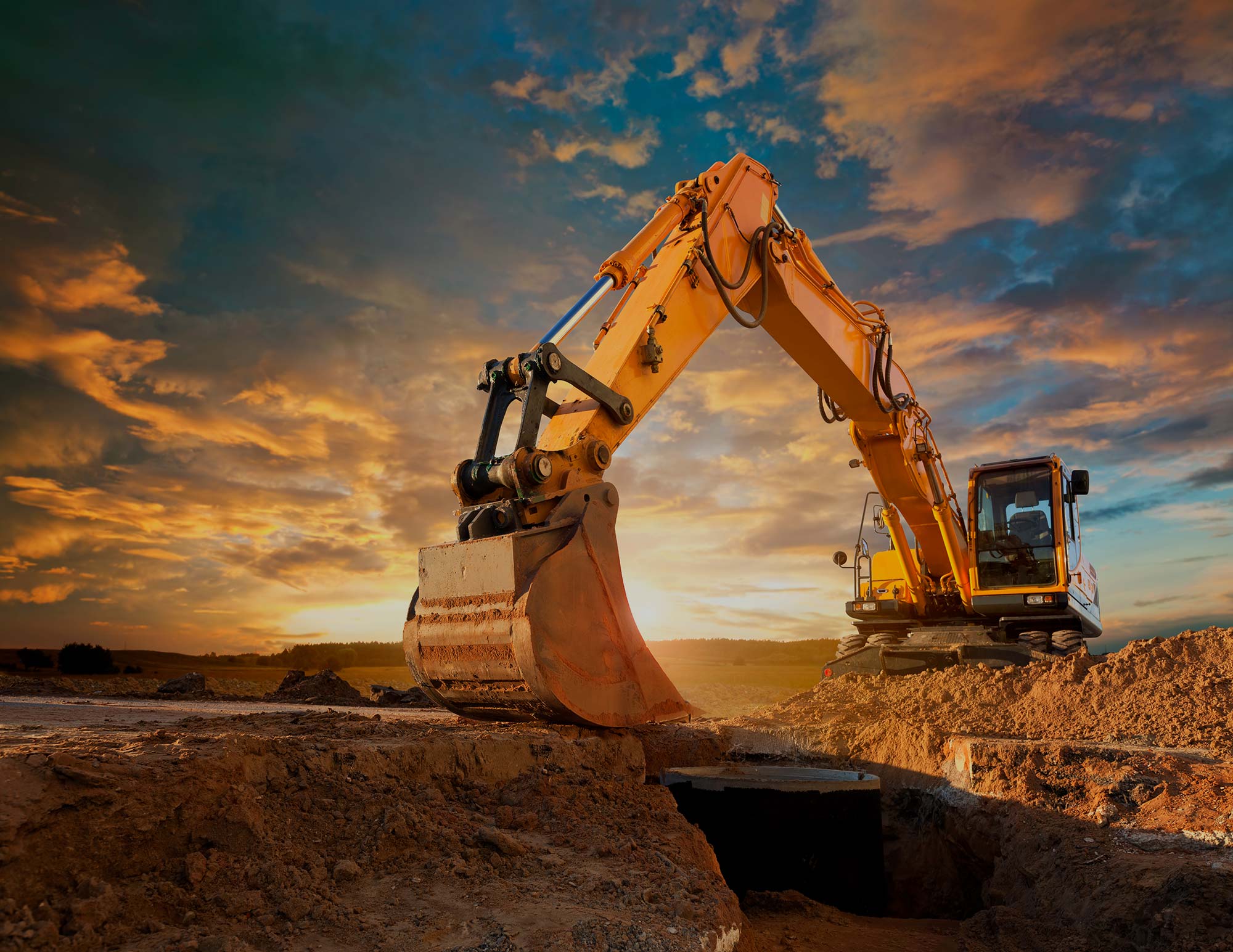 A yellow digger sitting on top of a pile of clay with the sun setting in the background