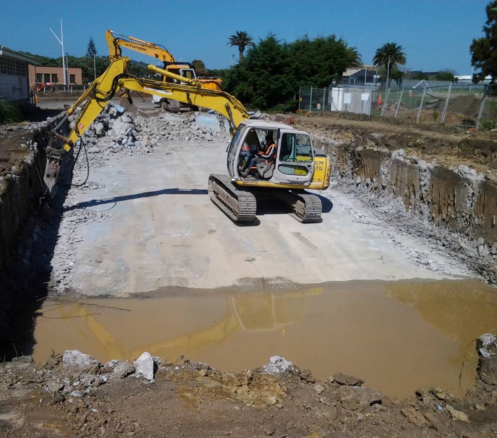 An excavator performing earthworks services with its digger at a residential worksite