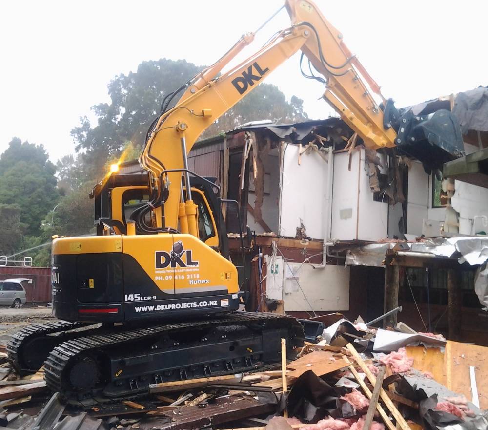 A yellow excavator demolishing the wall with its digger claw of a residential property