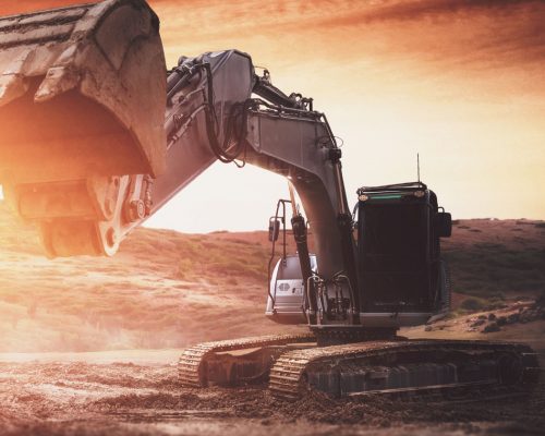 A black excavator with it's digger towards the camera digging at sunset