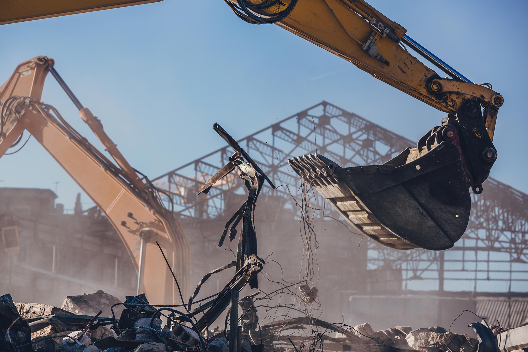 An excavator arm amidst debris with the structure of an industrial building in the background