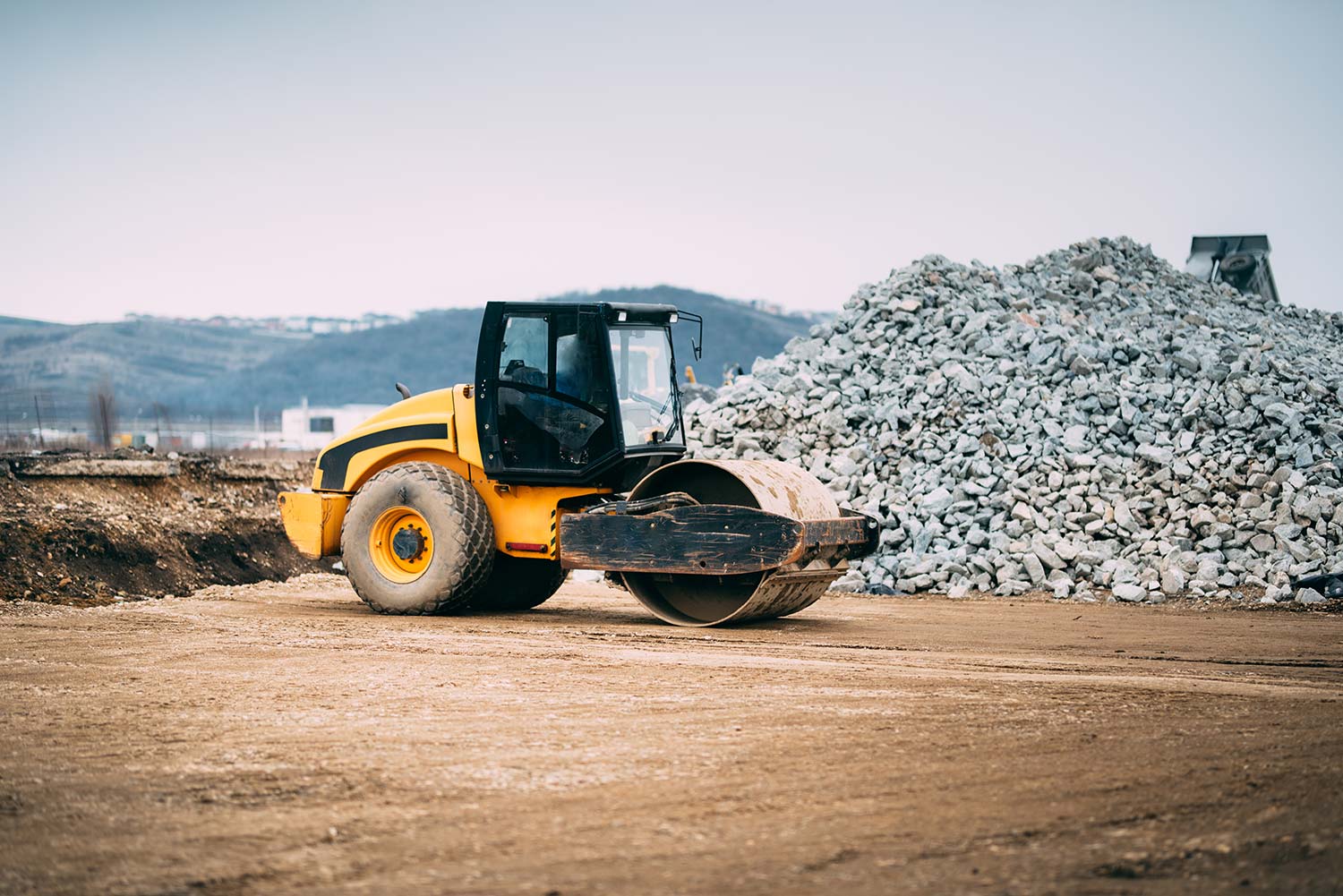 A road roller operating in front of a pile of rubble and debris